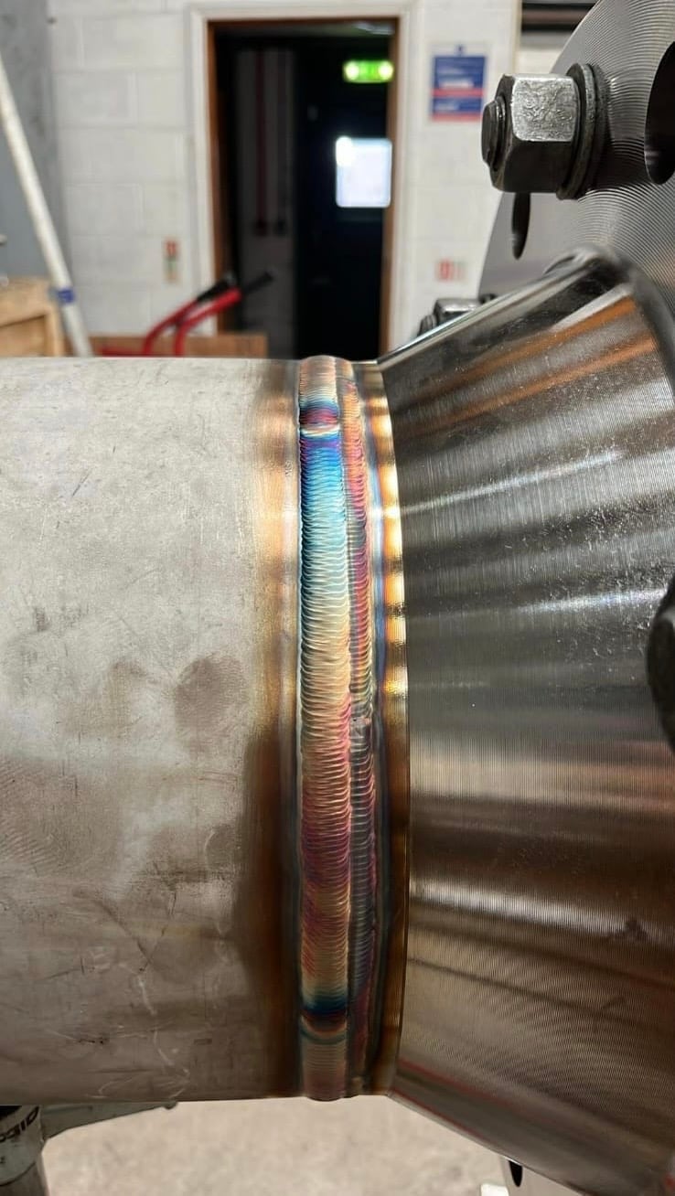 Close-up of welded metal joint with colorful wire wrapping showing different weld passes in an industrial workshop