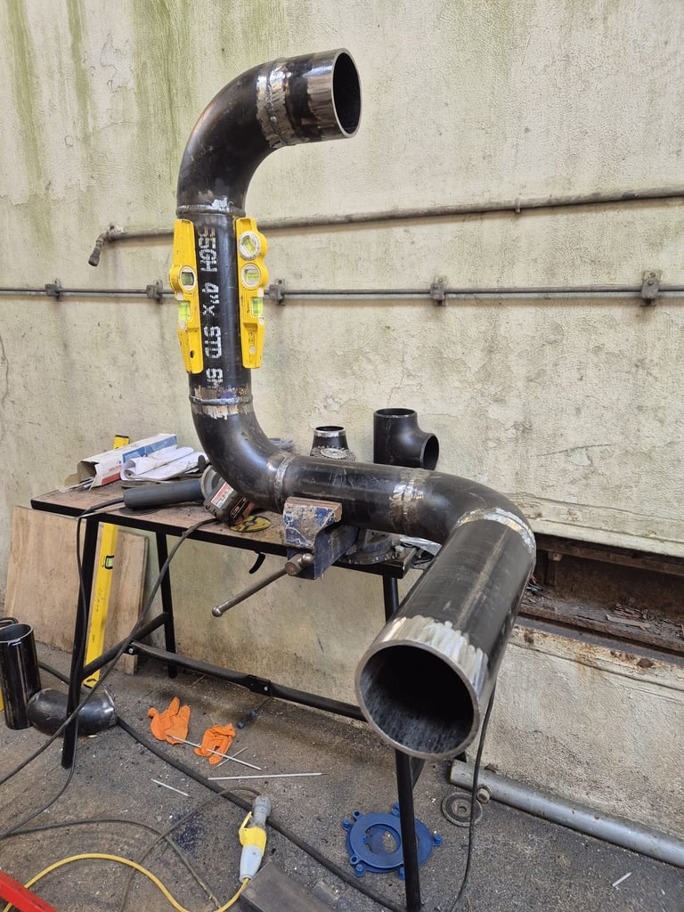 Industrial pipe bending machine with black metal pipes mounted on yellow and black metal frame against concrete wall