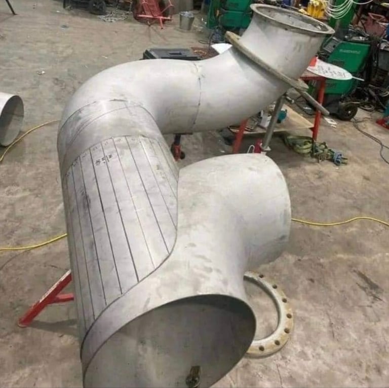 Large white metal cylindrical pipe sections connected at angles in an industrial or construction yard setting