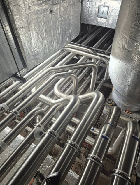 Industrial stainless steel pipes and tubing installed in a mechanical room with insulation on walls