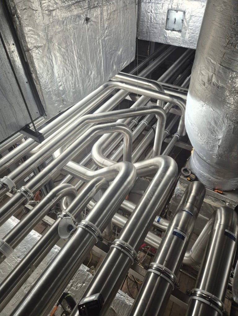 Industrial stainless steel pipes and tubing installed in a mechanical room with insulation on walls